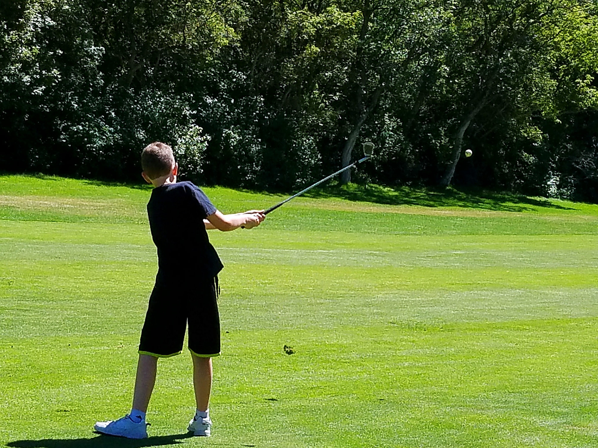 From behind action shot of golf ball after being hit by young golfer on green.